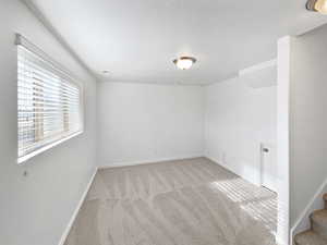 Unfurnished room with a textured ceiling, light carpet, visible vents, baseboards, and stairway