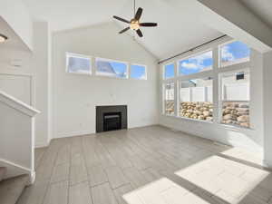 Unfurnished living room with baseboards, a ceiling fan, a tiled fireplace, stairs, and high vaulted ceiling