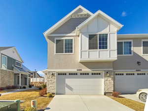 View of front facade featuring an attached garage, stone siding, concrete driveway, and stucco siding