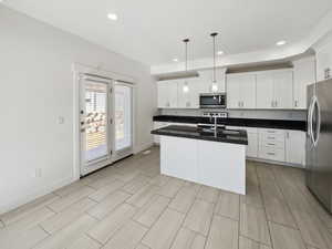 Kitchen with stainless steel appliances, a sink, white cabinetry, baseboards, and dark countertops