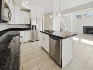 Kitchen with a fireplace, appliances with stainless steel finishes, open floor plan, white cabinetry, and a sink