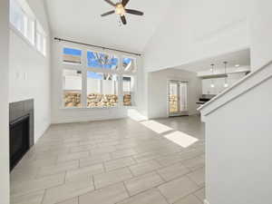 Unfurnished living room with high vaulted ceiling, a tiled fireplace, a ceiling fan, and a healthy amount of sunlight