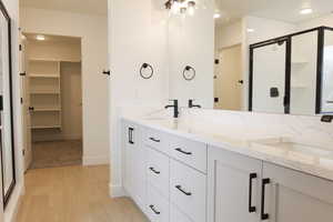 Full bathroom featuring a walk in closet, wood finished floors, a stall shower, and a sink