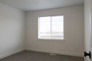 Spare room featuring plenty of natural light, dark colored carpet, and visible vents