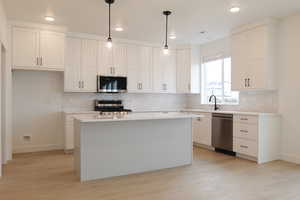 Kitchen with light wood-type flooring, baseboards, white cabinets, and appliances with stainless steel finishes