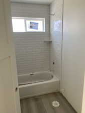 Bathroom featuring tub / shower combination, wood finished floors, and a healthy amount of sunlight