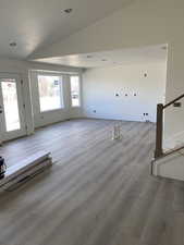 Unfurnished living room featuring lofted ceiling, stairs, and wood finished floors