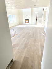 Unfurnished living room with a fireplace, light wood-style flooring, a textured ceiling, and stairs