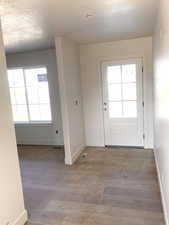 Doorway with a textured ceiling, baseboards, and wood finished floors