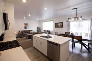 Kitchen with dark wood finished floors, dishwasher, light countertops, white cabinetry, and a sink