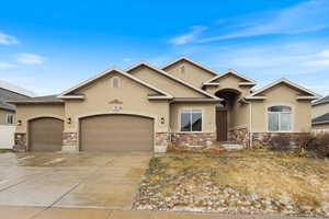 View of front of house with a garage, stone siding, concrete driveway, and stucco siding