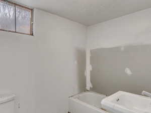 Bathroom featuring a sink, a textured ceiling, toilet, and a bath