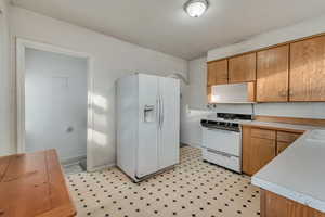 Kitchen featuring brown cabinetry, white appliances, light countertops, and light floors