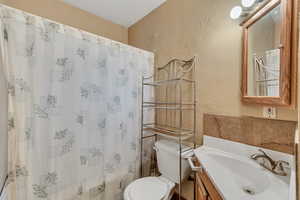 Bathroom with toilet, a textured wall, a shower with shower curtain, and vanity