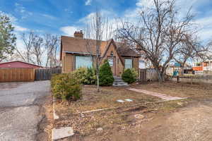 View of front of house featuring brick siding, fence, a chimney, and roof with shingles