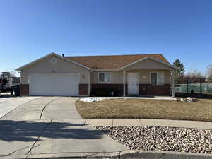 Ranch-style home with a garage, brick siding, concrete driveway, fence, and stucco siding