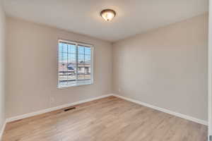 Empty room featuring light wood-style flooring, visible vents, and baseboards