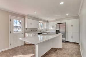 Kitchen featuring white cabinets, stainless steel appliances, crown molding, light countertops, and backsplash