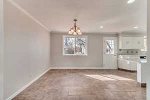 Unfurnished dining area featuring ornamental molding, recessed lighting, a notable chandelier, and baseboards