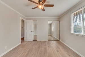 Unfurnished bedroom with light wood-style floors, crown molding, baseboards, and two closets