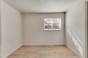 Unfurnished room with light wood-style flooring, baseboards, and a textured ceiling