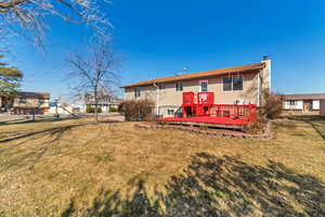 Rear view of property featuring a chimney, a deck, and a lawn