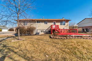 Back of property featuring a chimney, central AC unit, a deck, and a lawn