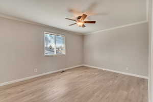 Empty room with crown molding, visible vents, light wood-style floors, ceiling fan, and baseboards