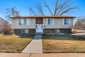 Raised ranch with a front lawn, a chimney, and brick siding