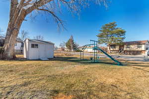 View of yard with an outbuilding, a shed, a playground, and fence