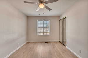 Unfurnished bedroom with a ceiling fan, a closet, light wood-style flooring, and baseboards