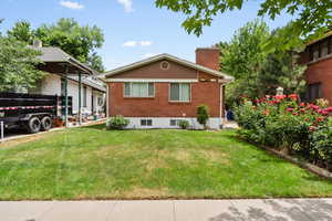 View of front of property featuring brick siding, a chimney, and a front yard
