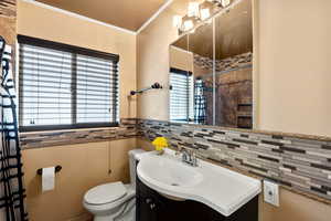 Full bathroom featuring tiled shower, vanity, crown molding, tile walls, and a wainscoted wall