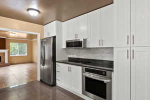 Kitchen with appliances with stainless steel finishes, tasteful backsplash, white cabinets, a stone fireplace, and open floor plan