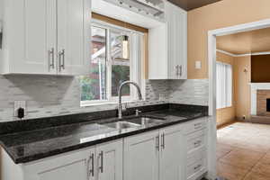 Kitchen with white cabinetry, dark stone countertops, and backsplash
