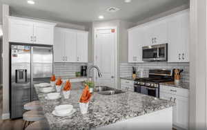 Kitchen featuring a sink, visible vents, white cabinets, appliances with stainless steel finishes, and a center island with sink