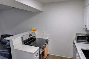 Kitchen featuring white cabinets, light stone counters, stainless steel appliances, and wood finished floors