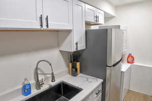 Kitchen with light stone counters, light wood finished floors, freestanding refrigerator, white cabinetry, and a sink