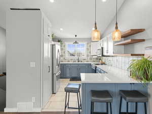 Kitchen featuring blue cabinetry, visible vents, appliances with stainless steel finishes, a sink, and a peninsula