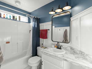 Full bath with a textured ceiling, toilet, vanity, wainscoting, and shower / bathtub combination with curtain