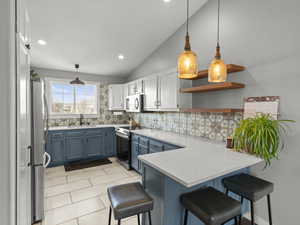 Kitchen featuring electric stove, blue cabinetry, refrigerator, a sink, and a peninsula