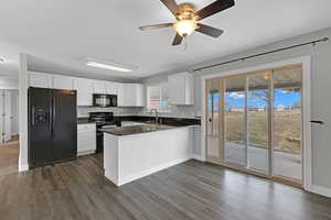 Kitchen featuring dark countertops, a peninsula, black appliances, white cabinetry, and a sink