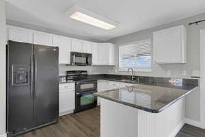 Kitchen featuring white cabinets, dark stone countertops, a peninsula, black appliances, and a sink