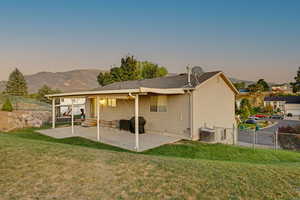 Back of property at dusk with entry steps, a lawn, cooling unit, and a fenced backyard