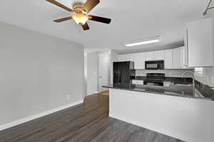 Kitchen featuring dark stone countertops, a peninsula, black appliances, white cabinetry, and a sink