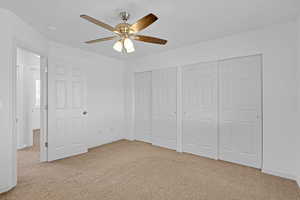 Unfurnished bedroom featuring light colored carpet, ceiling fan, and two closets