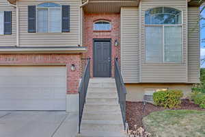 View of exterior entry featuring driveway, brick siding, and an attached garage