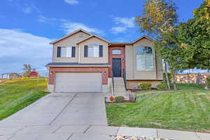 Bi-level home with a garage, concrete driveway, brick siding, and a front lawn