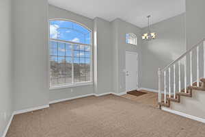 Foyer entrance featuring a high ceiling, carpet flooring, baseboards, stairway, and an inviting chandelier