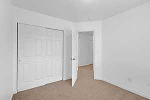 Unfurnished bedroom featuring baseboards, a closet, and light colored carpet